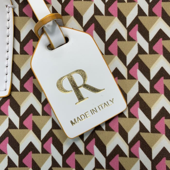 白色 Roberta Pieri 行李牌的特写，上面有金色字母“R”和“MADE IN ITALY”字样，贴在带有棕色、米色和粉色几何图案的迷你行李袋上。