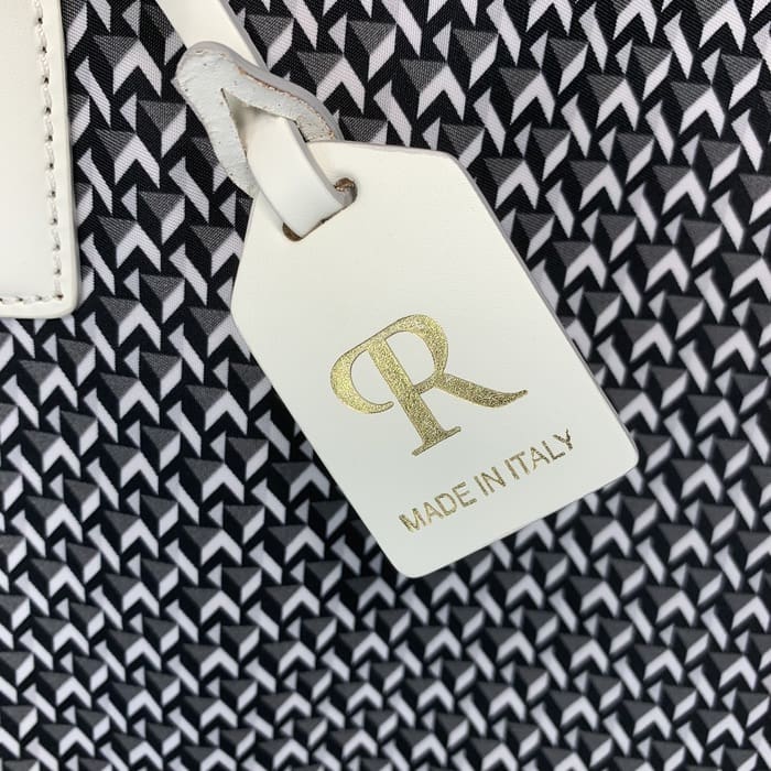 黑色和白色几何织物的背景上悬挂着带有金色字母“R”和“MADE IN ITALY”字样的白色皮革 ROBERTA PIERI 标签。